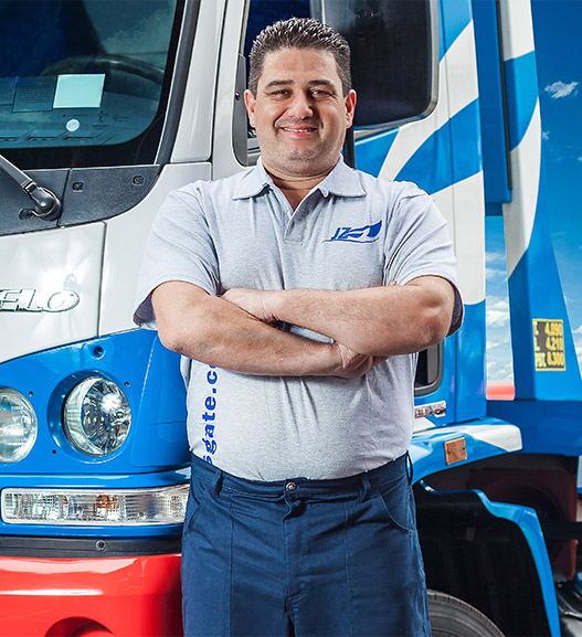 Motorista da JZ Resgate de uniforme, de braços cruzados, em frente a um caminhão da frota